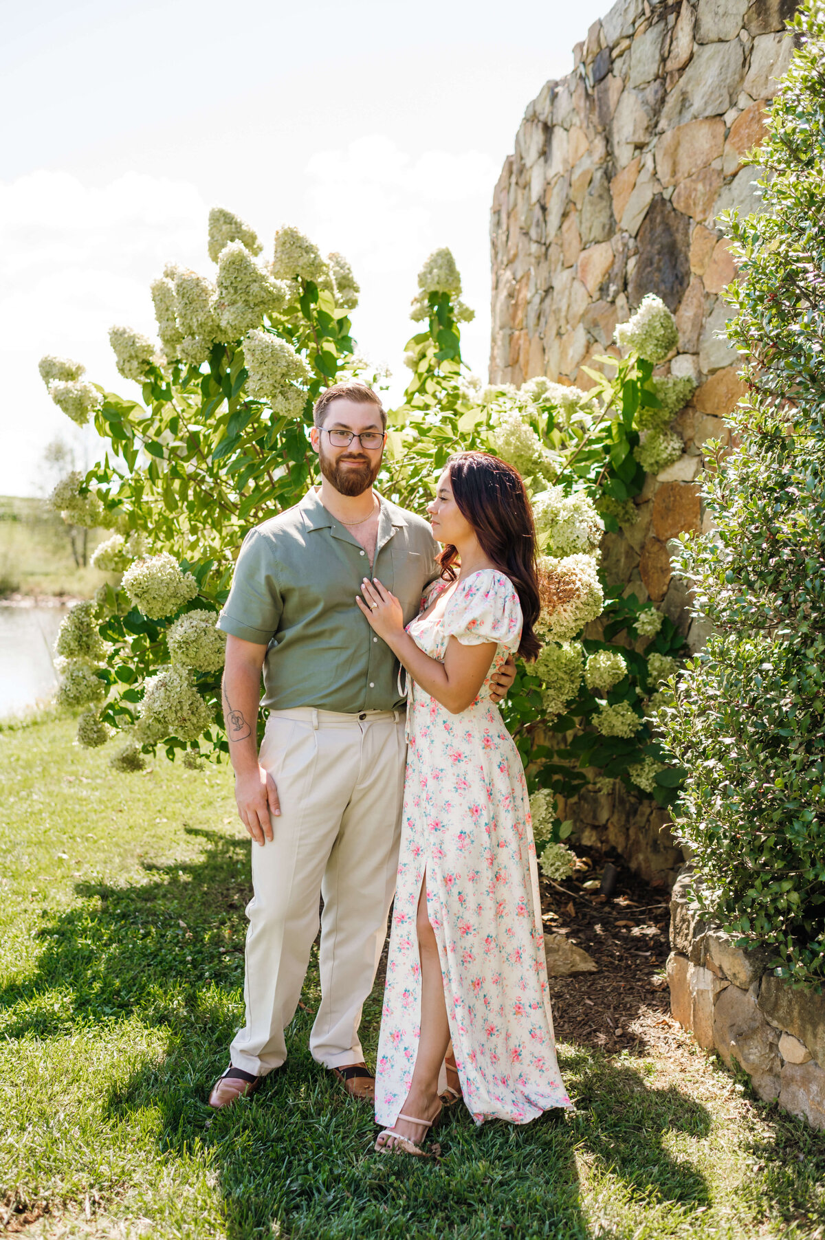 woman holding her fiances chest as she smiles up to him in front of a hydrangea bush at stone tower winery wedding venue