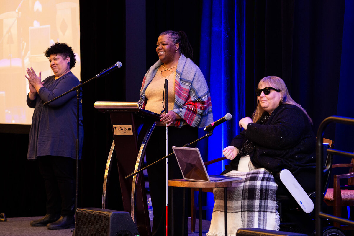 a black woman standing and a woman in a wheelchair on a stage speaking to attendees during a 2-day conference at the Westin Hotel.  Captured by Ottawa Event Photographer JEMMAN Photography COMMERCIAL