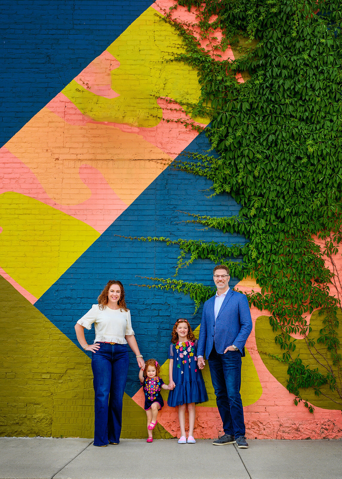 Family of 4 in front of a colorful mural with green vines