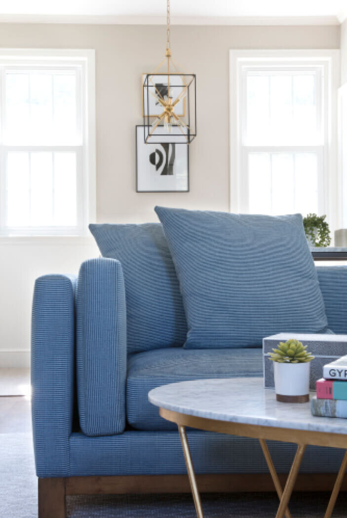 Interior decorators in Westwood design a family room with a bright blue Kravet sofa, a brass and marble coffee table, and stylish yet family-friendly decor.