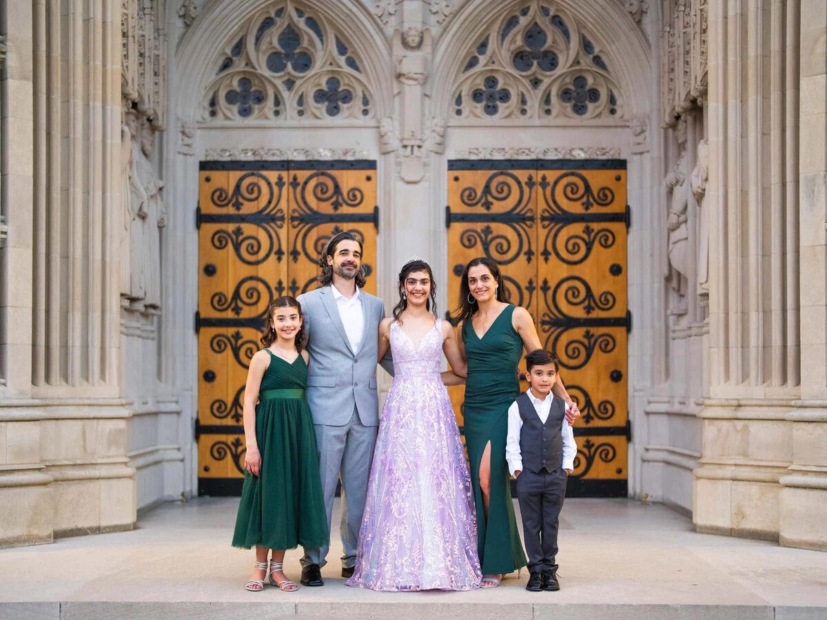 Parents and their three kids smiling and standing in front of a grand doorway.