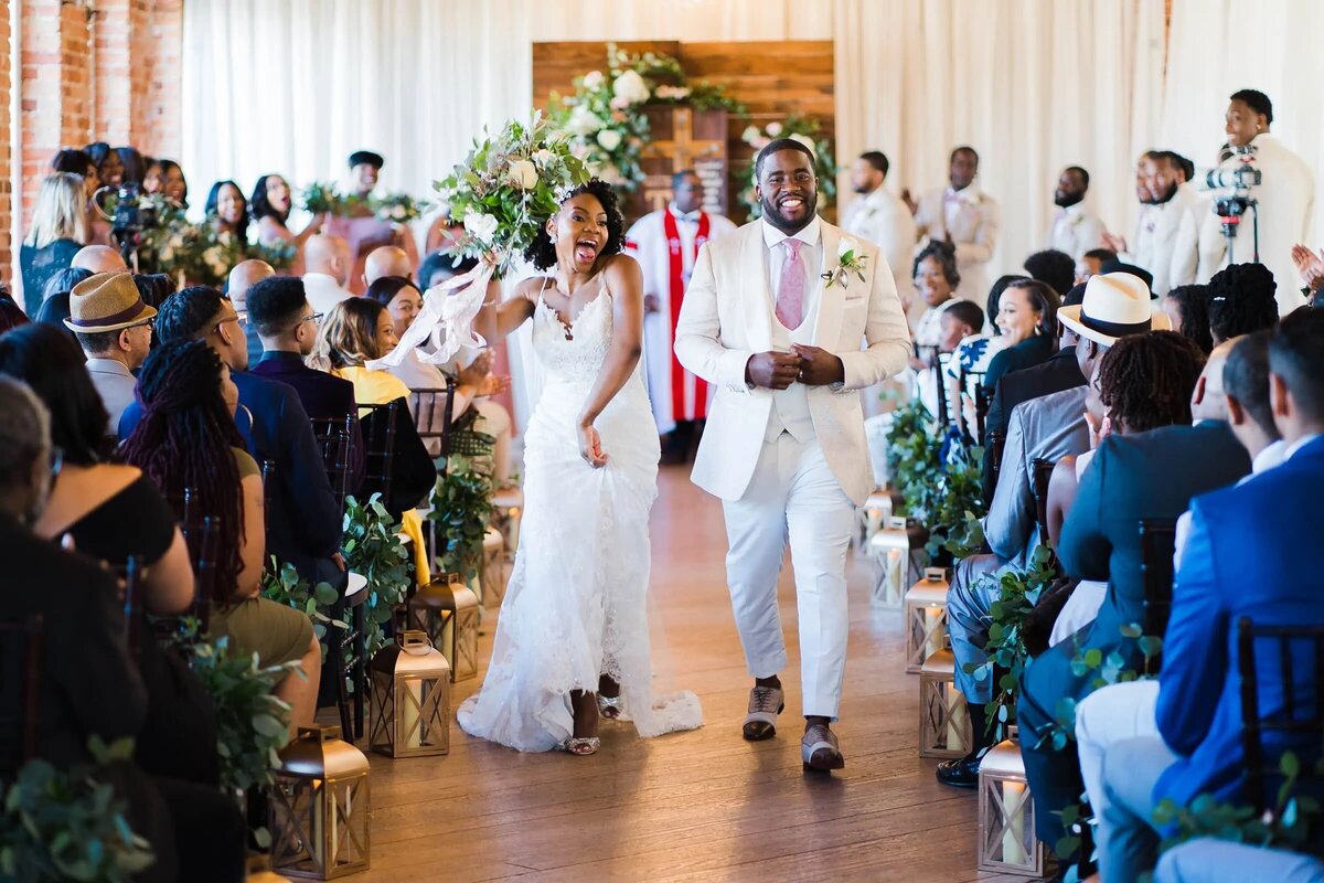 A bride and groom make their grand exit down the aisle, smiling exuberantly as guests line the path on both sides.