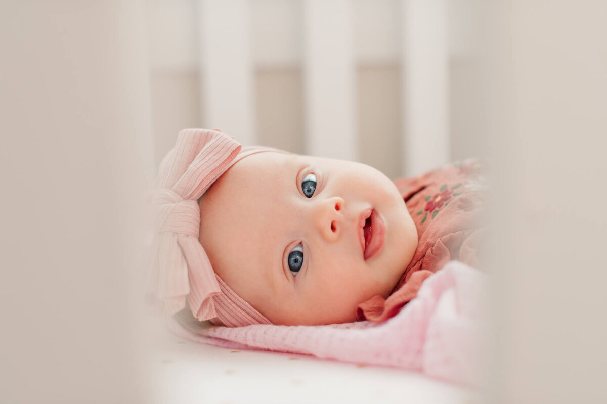 Newborn baby peeking through the crib railing with beautiful blue eyes