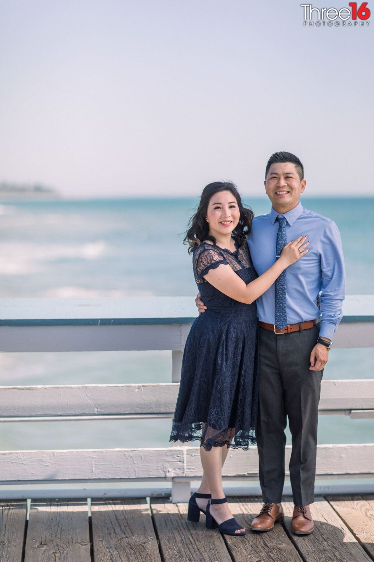 With the ocean behind them engaged couple pose together on the San Clemente Pier