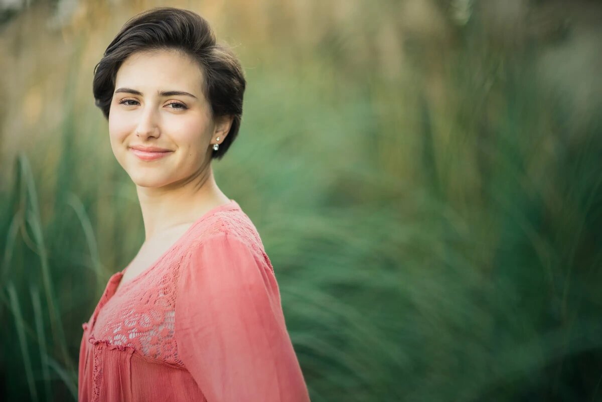 A teenager standing in tall grass slightly smiling.