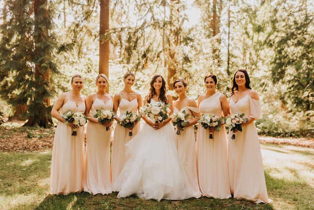 bride and bries maids wearing long blush dresses and holding garden flower arrangements in white and blush
