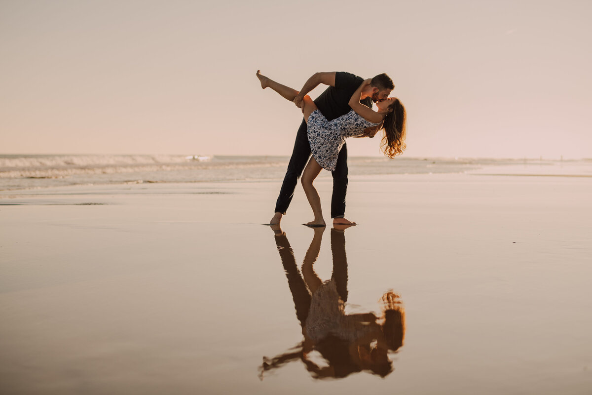 bride and groom kiss and dip during sunset engagement shoot on the beach shot by philadelphia wedding photographer  alex medvick