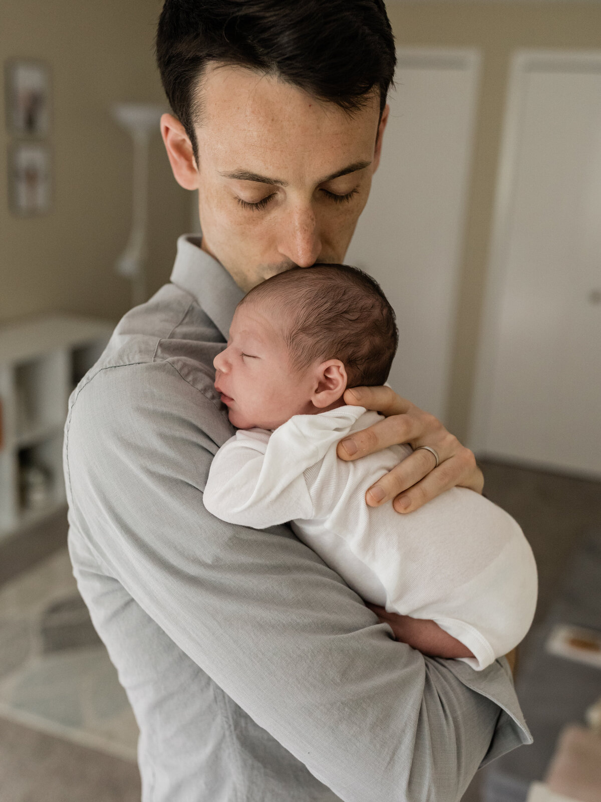 dad kissing newborn baby boy in white onesie