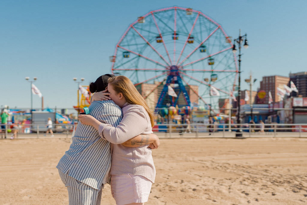 couple hugging each other on the beach with a ferris wheel behind them
