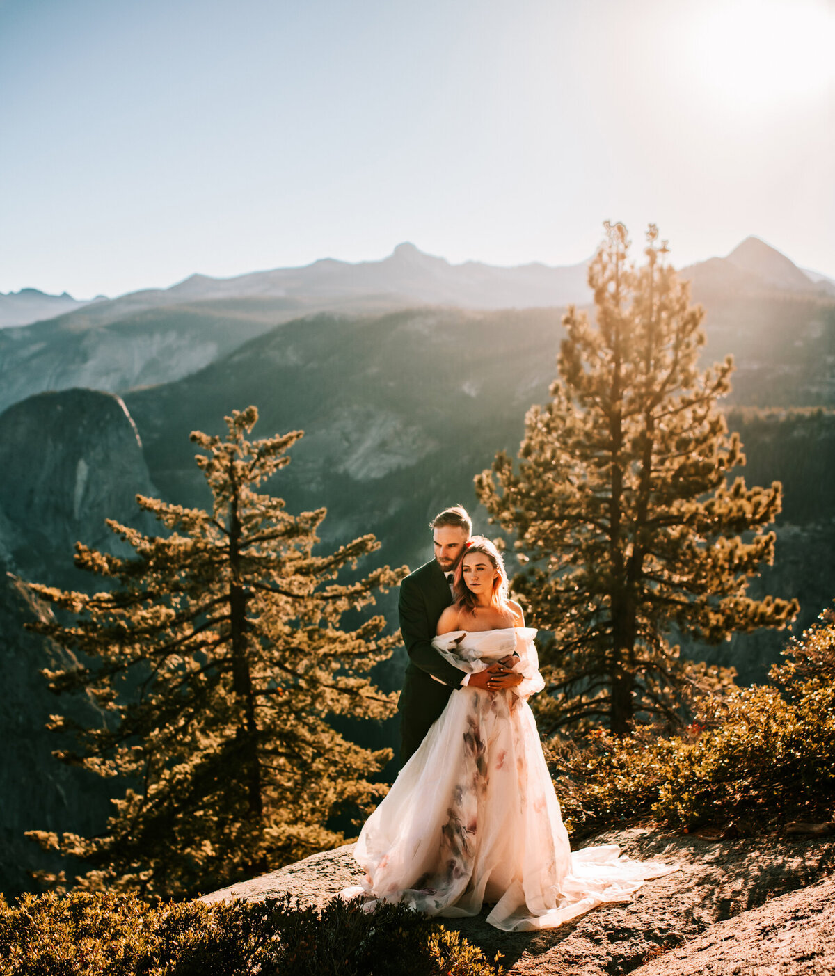 Couples Photography, Man in a blue suit holds onto woman in a wedding dress with the mountains of Yosemite behind them.