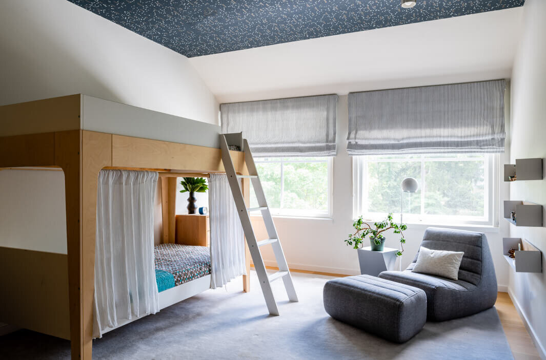 Best Boston interior decorators design a kids' bedroom with navy blue constellation wallpaper on the ceiling, bunk beds, and a modern lounge chair for a cozy retreat.