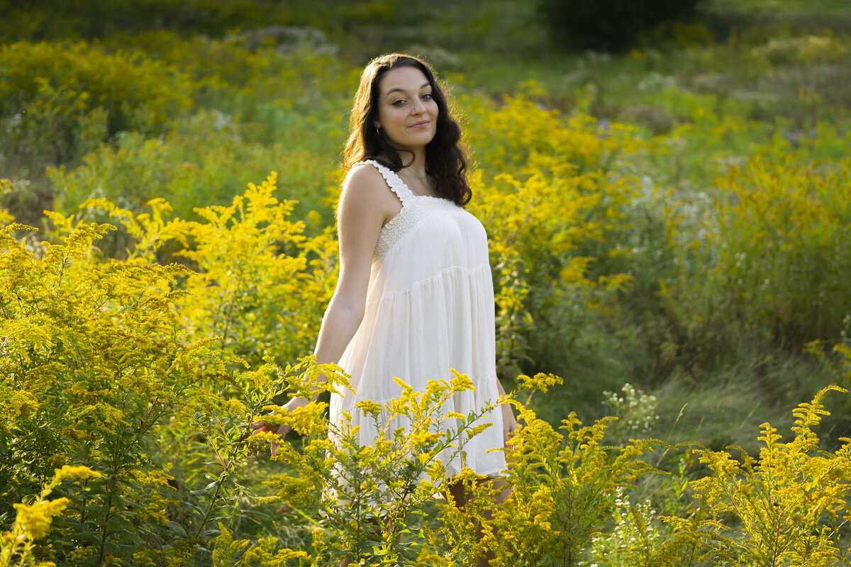 Senior portrait of a young woman in a white dress posing in a bed of flowers