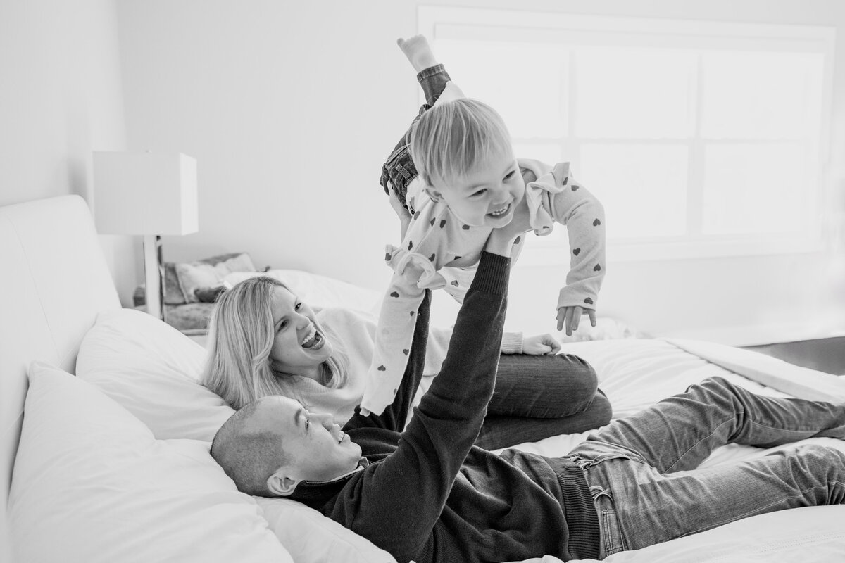 Family of Mom, Dad, and toddler doing airplane on bed