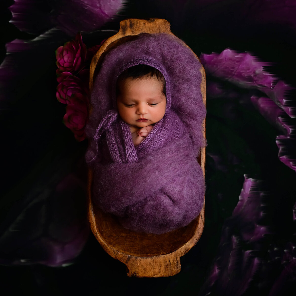 Newborn baby girl wrapped in purple sleeping in a long bowl on a floral purple backdrop, photographed by E. Benecki Photography.