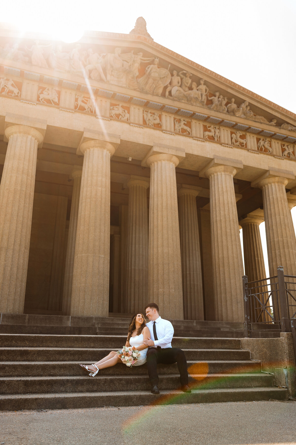 Bright sunny flare on the steps of the Parthenon in Nashville with Bride and groom Sitting