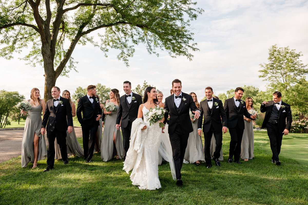 Bride and groom and large wedding party walk outside