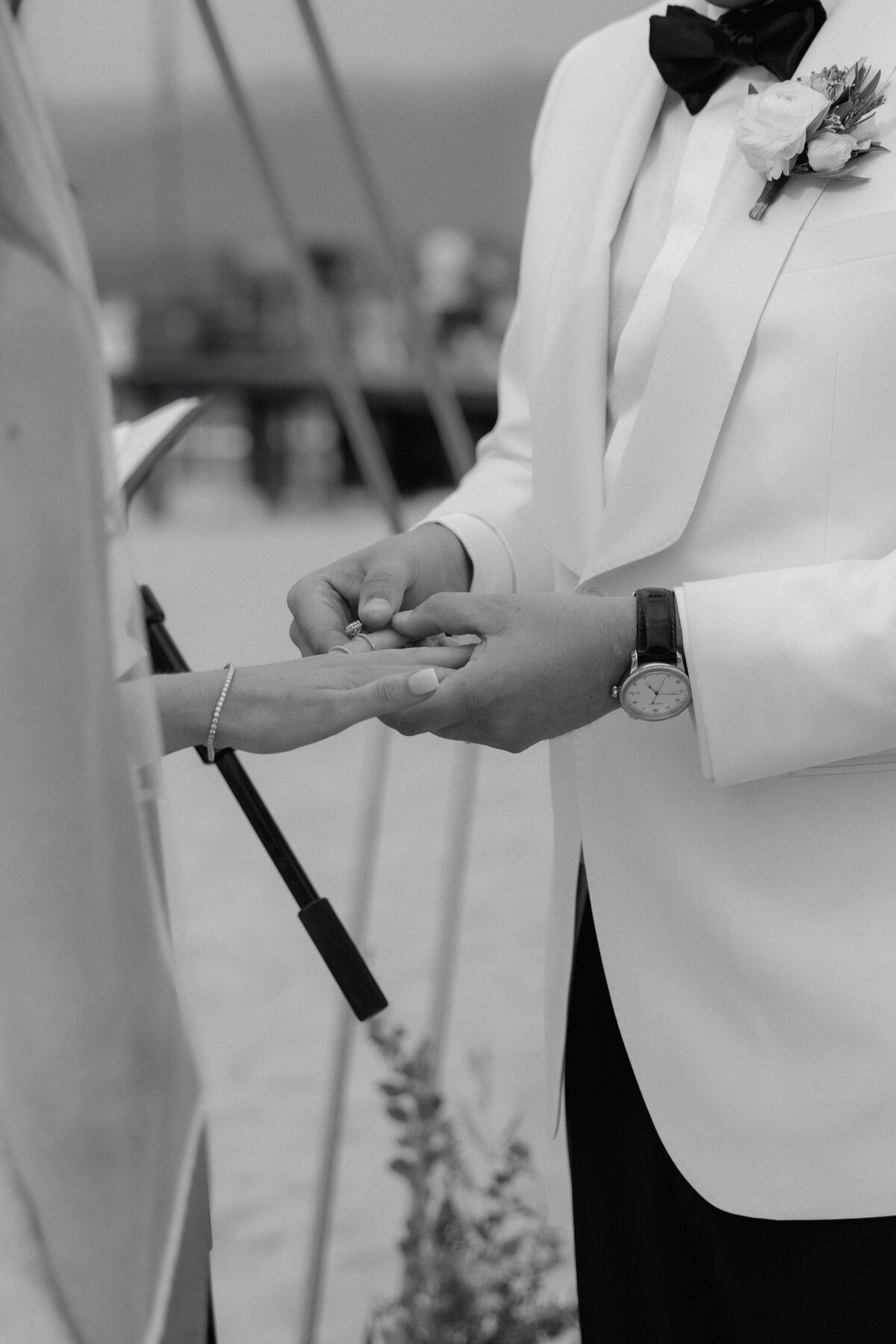 A timeless, intimate black and white photograph documenting a groom placing a wedding ring on the bride’s finger during their vows. Captured in a storytelling style by a luxury wedding photographer, highlighting elegant wedding-day details and emotional connection.