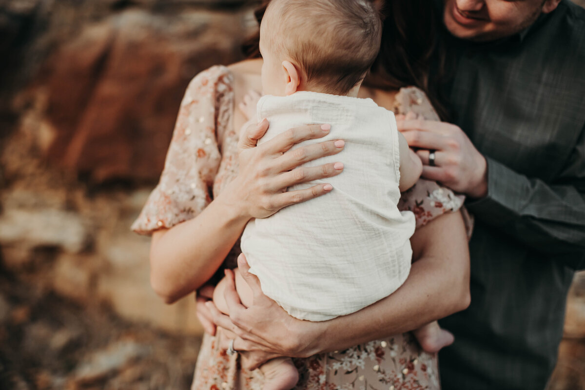 Close up of the embrace of mom and dad with 6 month old boy.