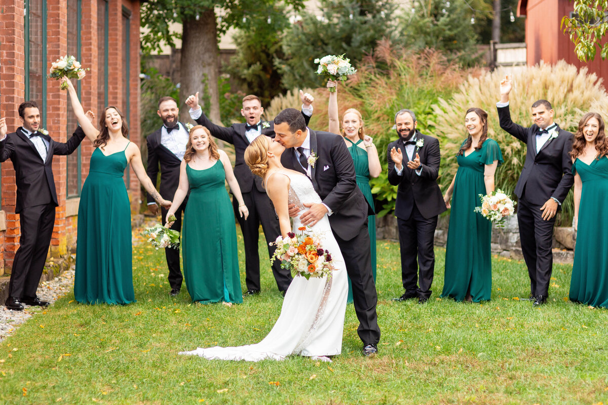 Bride and groom kiss as their wedding party cheers.