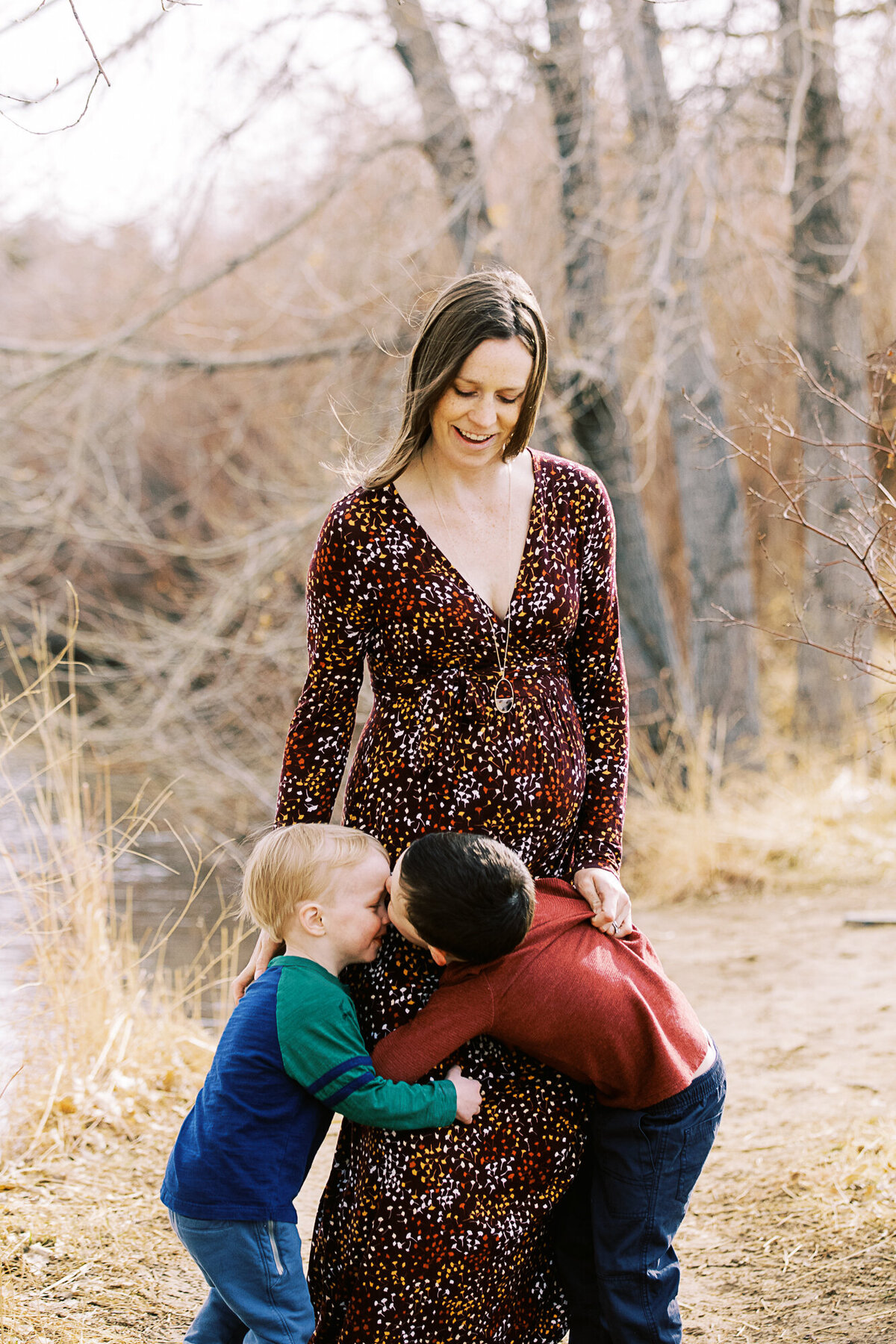 a pregnant mom in a fall-toned dress looks down at her goofy young sons who stand beneath her little baby bump