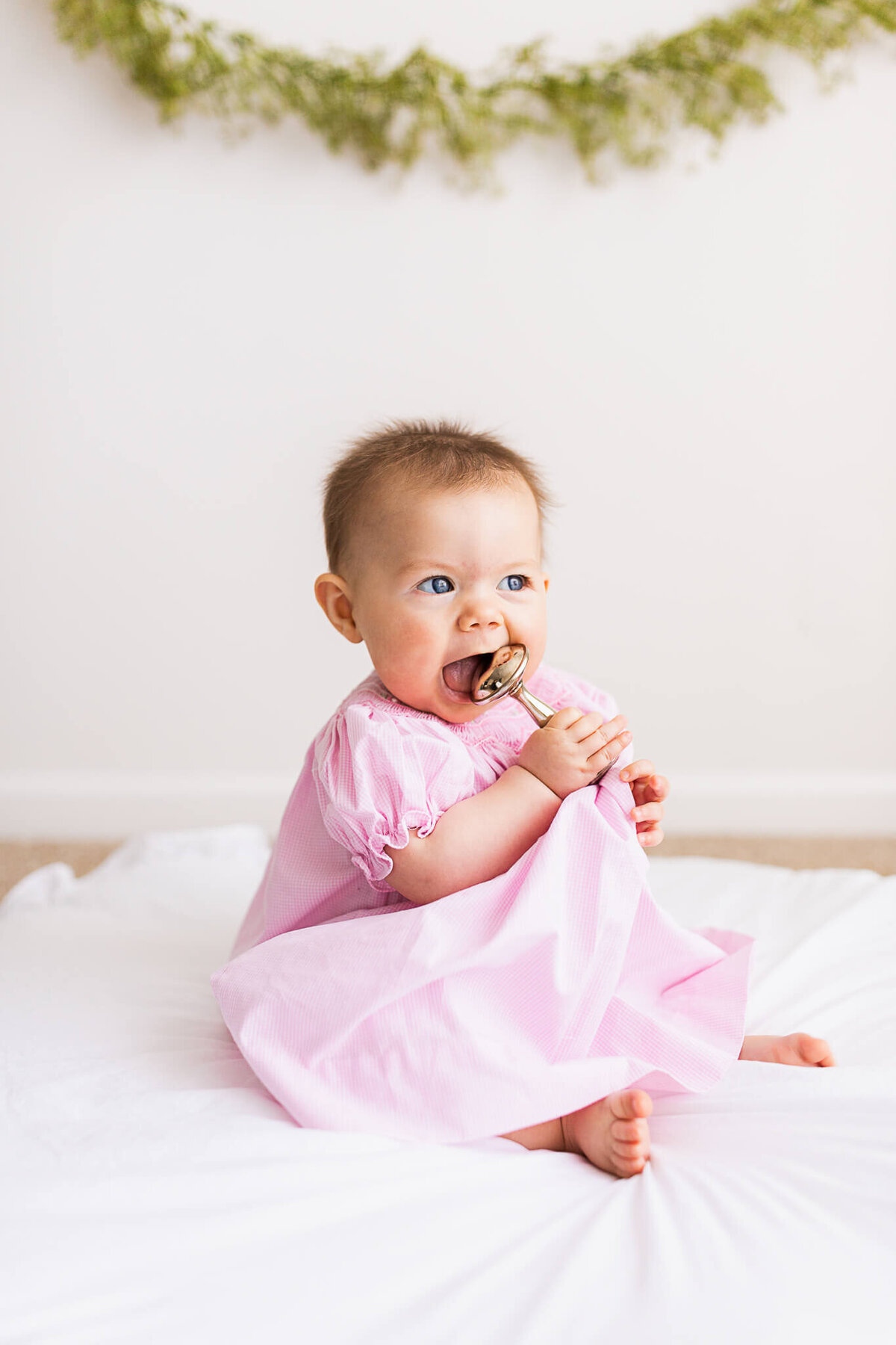 A six month old sitting by herself and putting a family heirloom rattle to her mouth