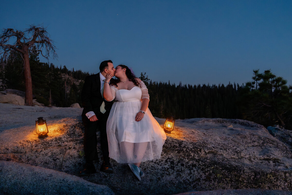 Bride and Groom eloping at Yosemite National Park Taft Point cliff during blue hour sitting on cliff and kissing with lanterns.