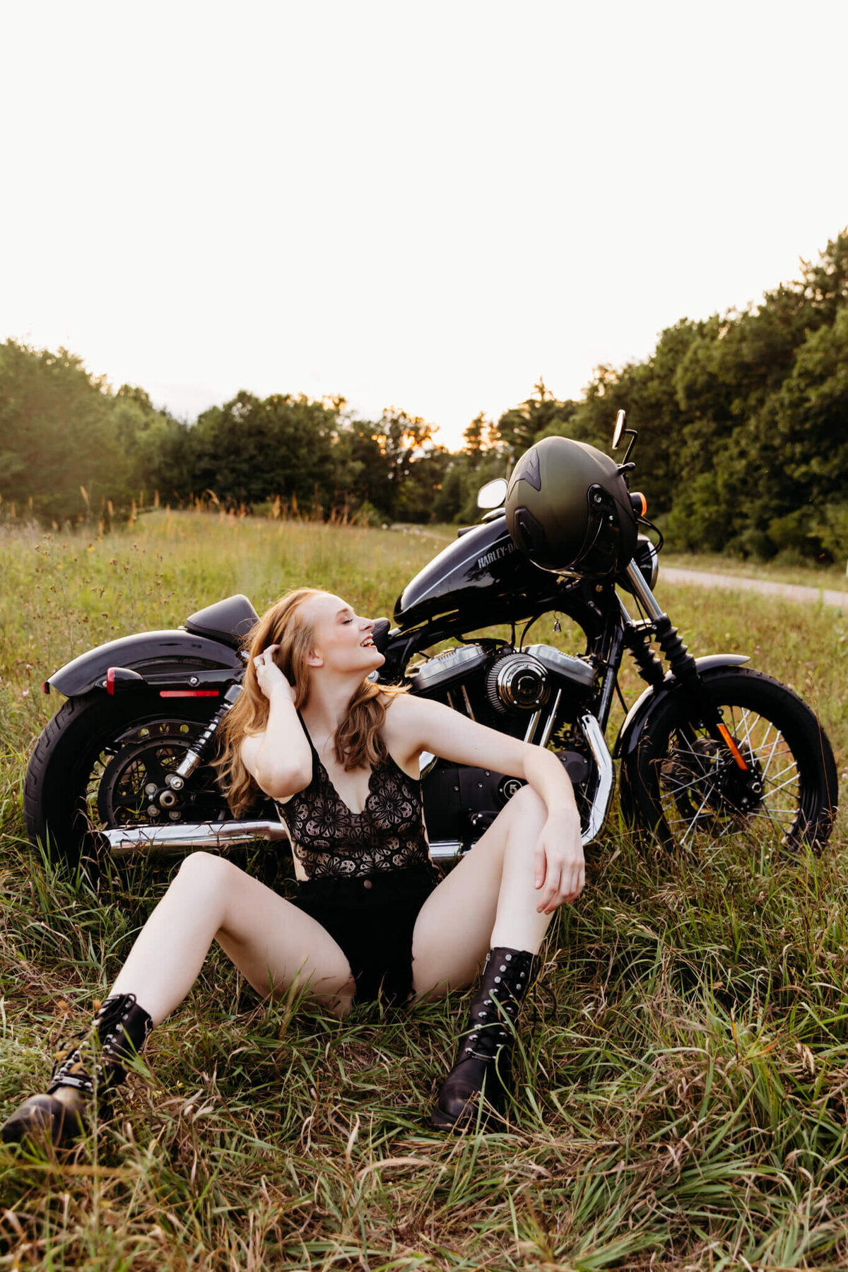 woman in black lace lingerie smiling and playing with her hair as she sits next to her motorcycle during her Oshkosh boudoir photo session