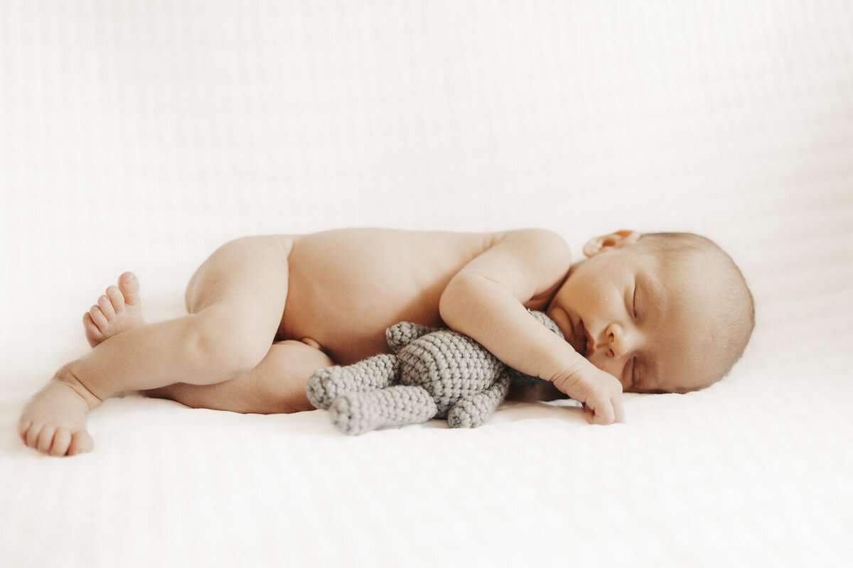 Sleeping newborn lying on his side, holding a grey teddy bear by newborn photographer in Tifton Georgia