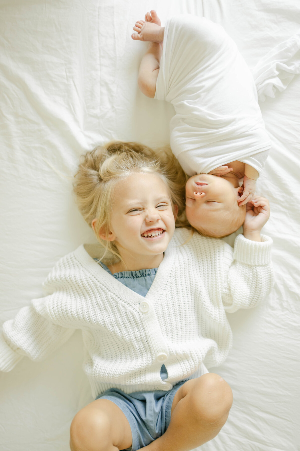 a little girl with her newborn baby brother laying in bed next to each other smiling