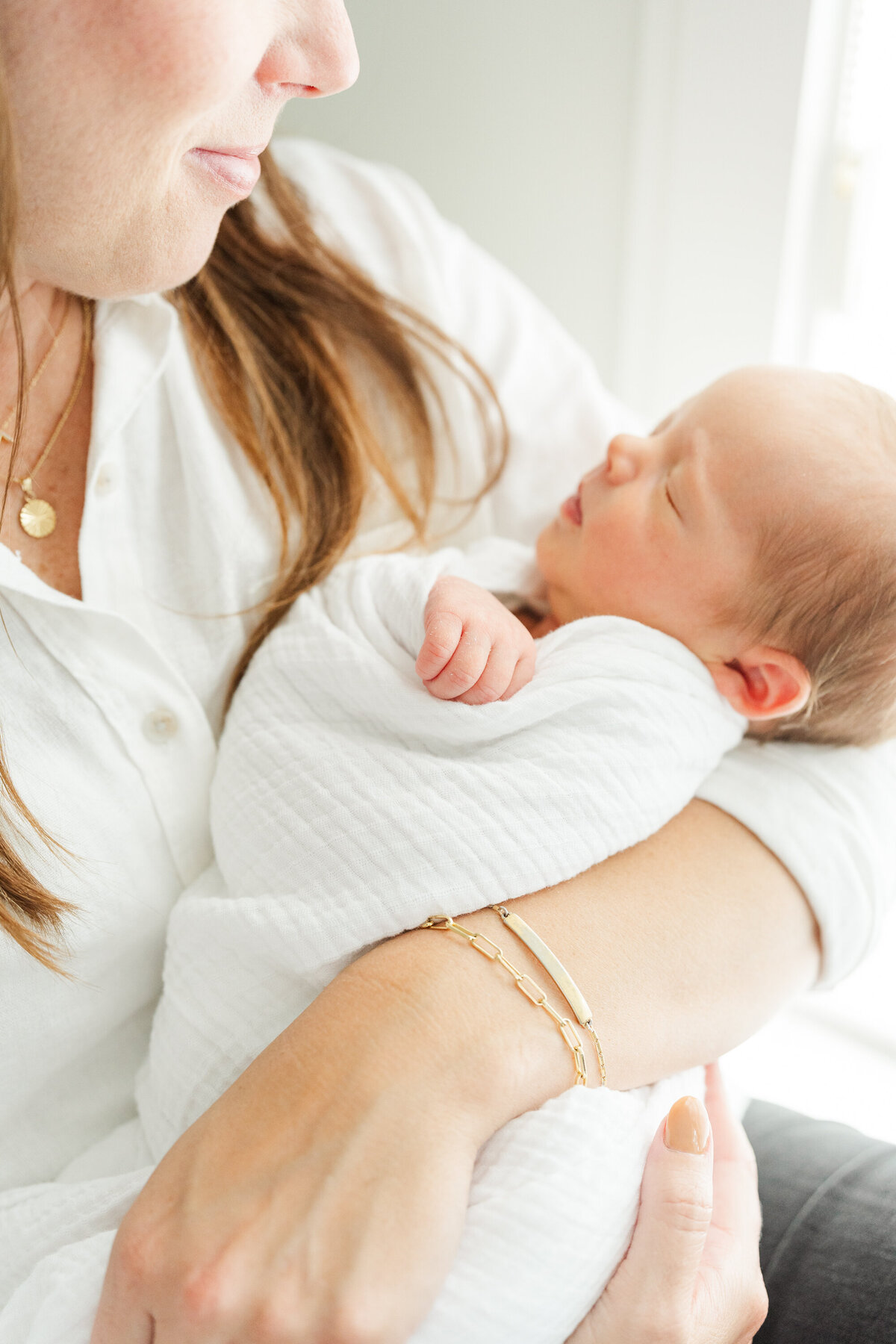 A mother lovingly gazes at her swaddled newborn, holding them close with a tender expression