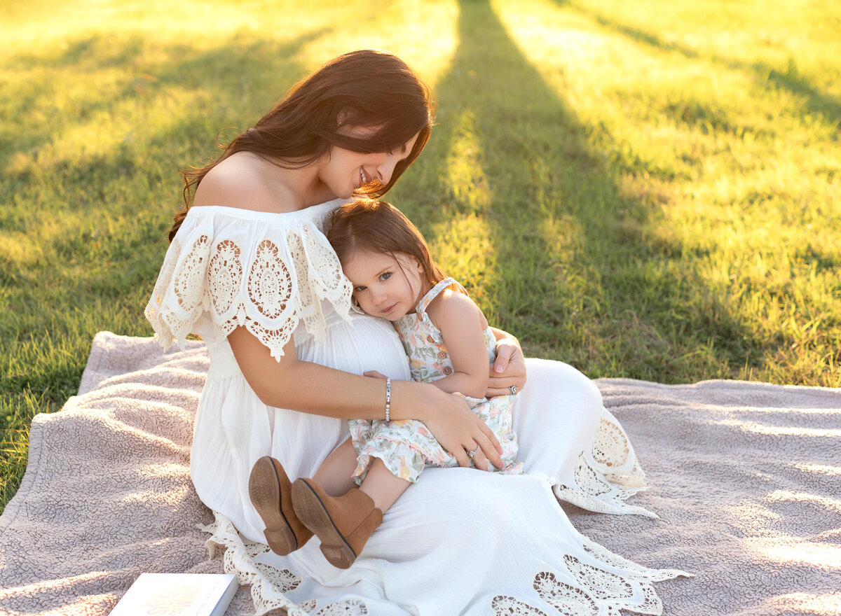 Heartwarming maternity image in Liberty Hill of a mother and toddler sharing a sweet moment in a sunny field, with mom in a white crochet-trim dress.
