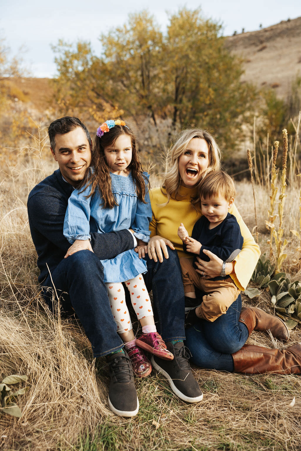 Two parents sitting in grass with kids in both of their laps.