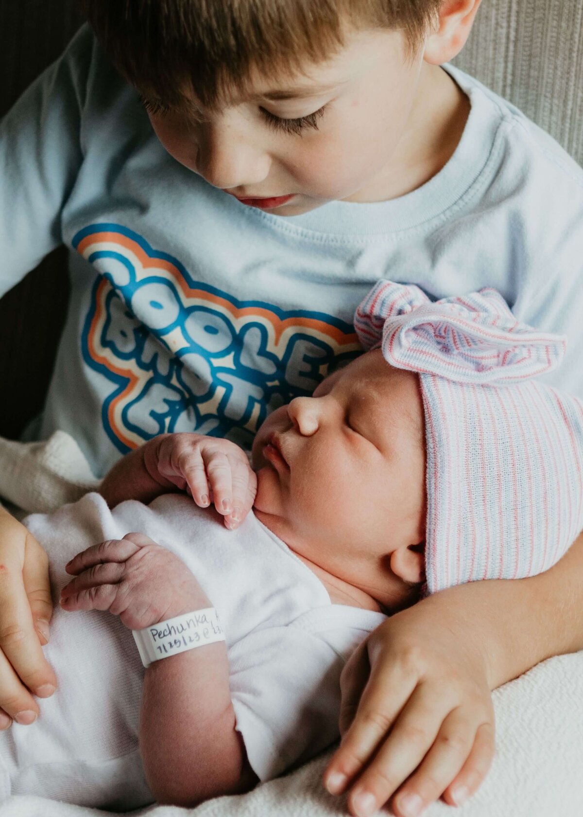 A boy lovingly cradles his new baby sister in his arms, captured by a Pittsburgh newborn photographer.