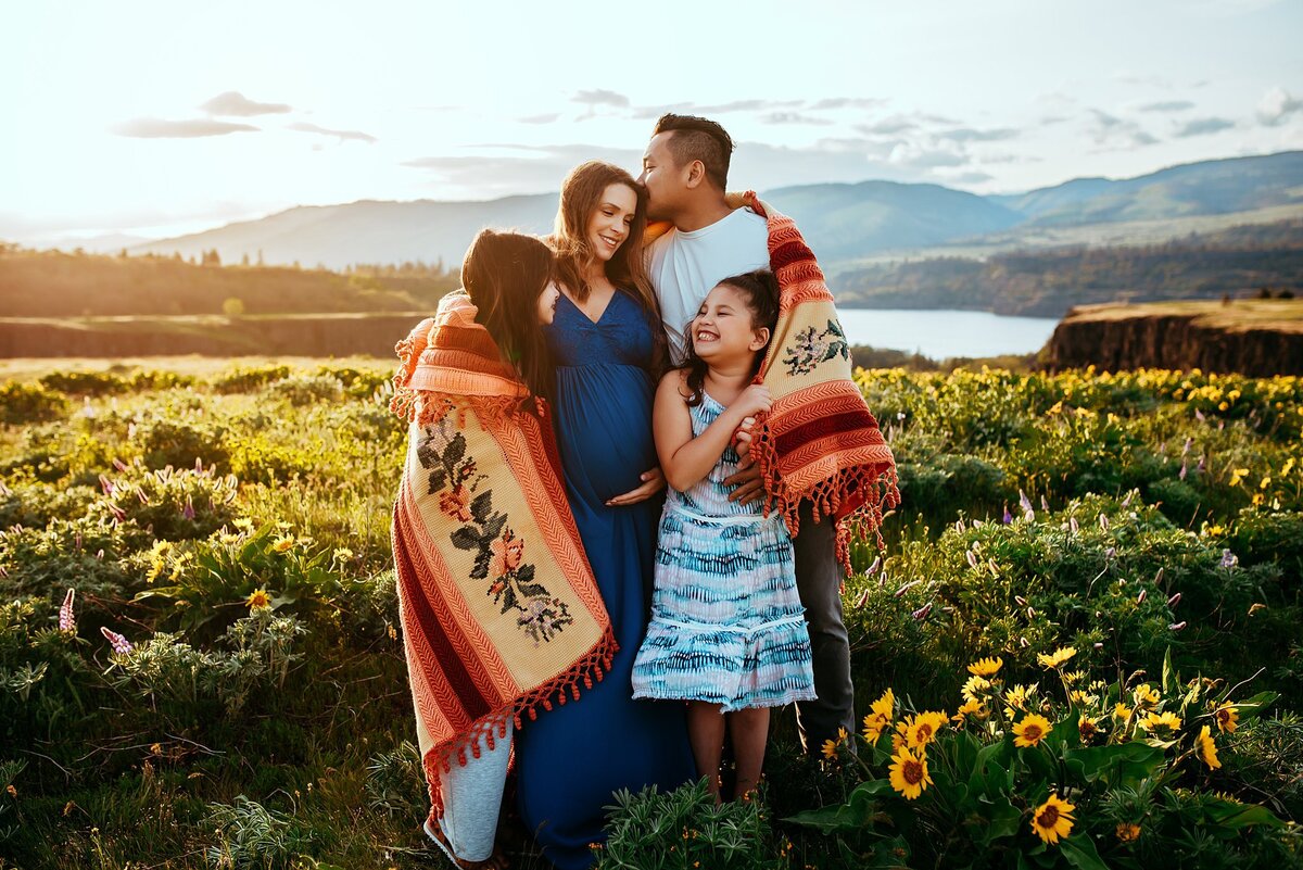 Mom, Dad and two sisters wrapped in a vintage blanket in a field of wildflowers at sunset