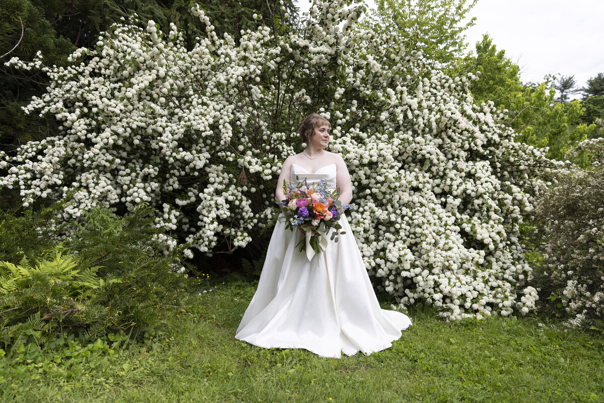bride holding her bridal bouquet in front of flowery bush Tyler Arboretum in Pennsylvania