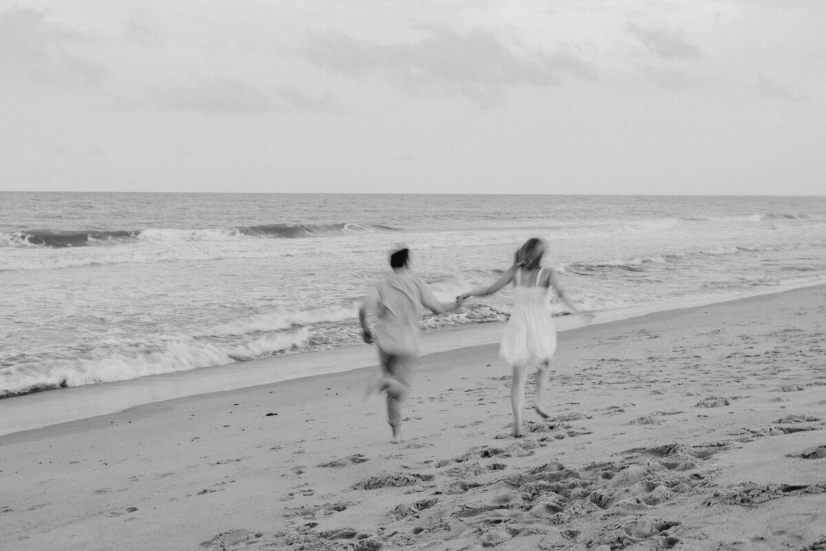 Couple running hand-in-hand on Wilmington beach, joyful engagement session
