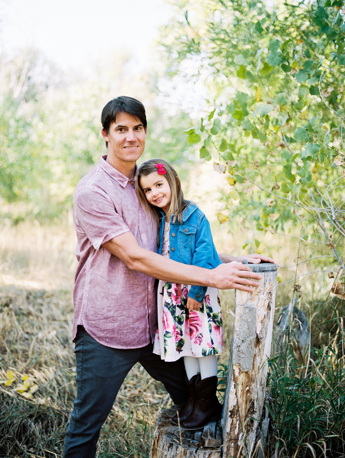 a girl stands on wooden tree while dad in pink supports her