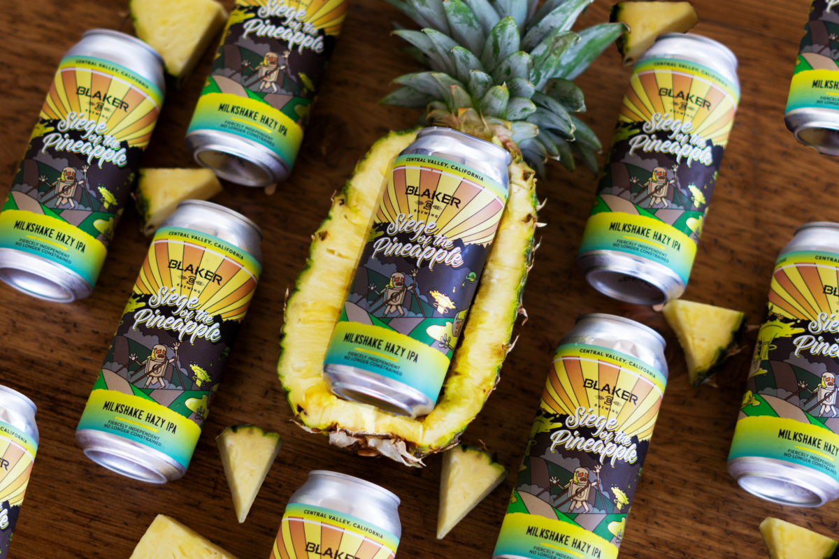 Siege of the pineapple Beer made by Blaker Brewing pictured inside a pineapple surround by other beer cans and pineapple chunks