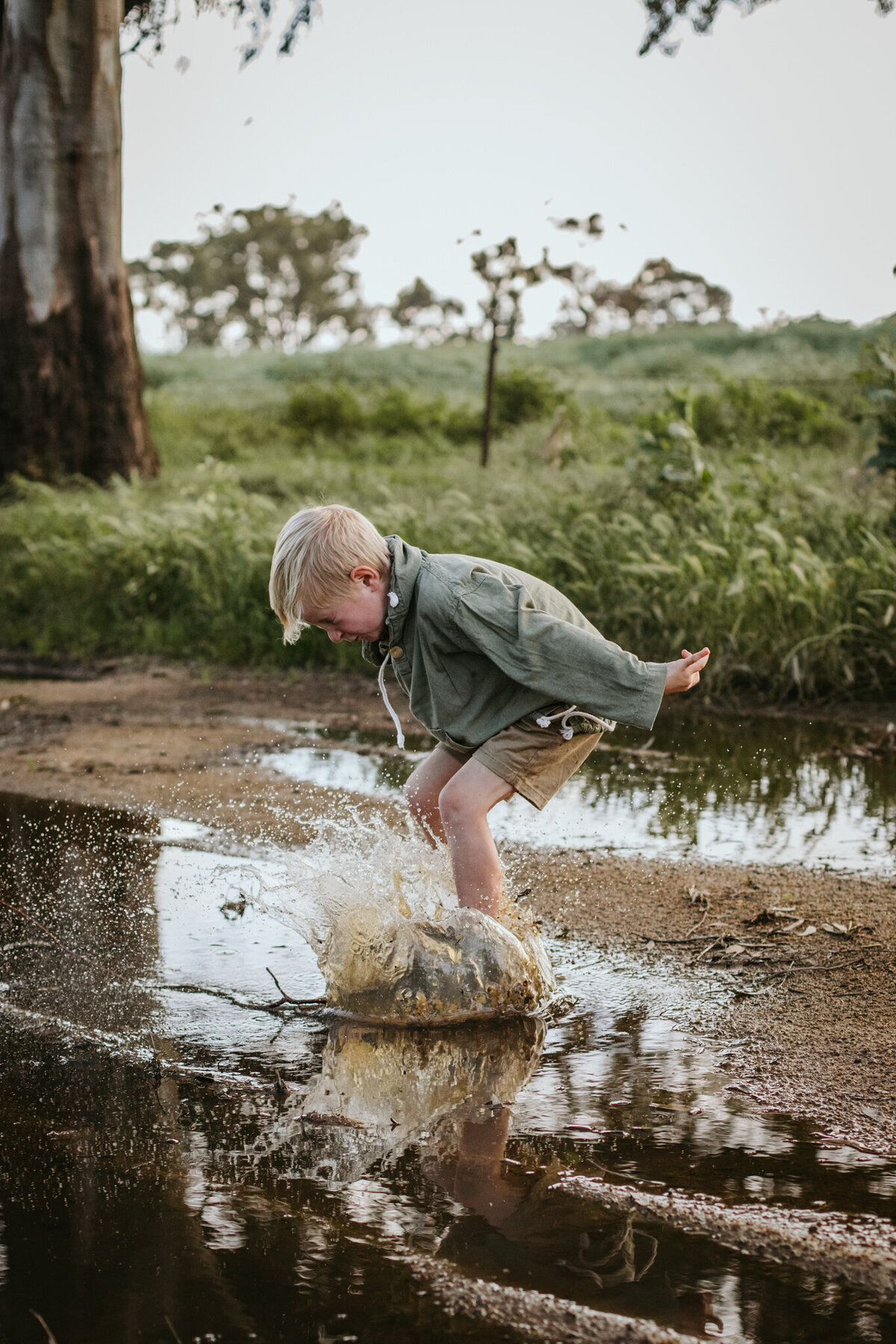 Candid moment of a 7-year-old jumping into a muddy puddle with anticipation.