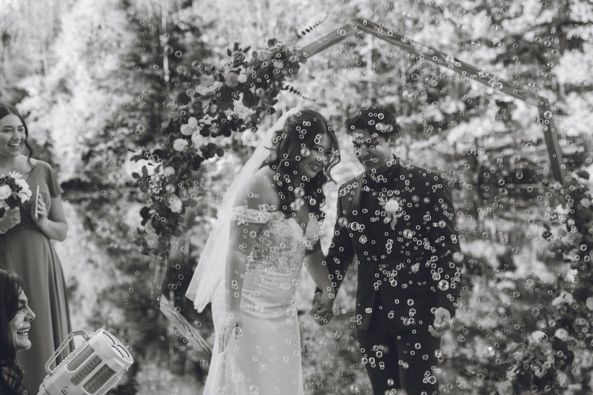 Black and white shot of the bride and groom kissing under a bubble send-off.