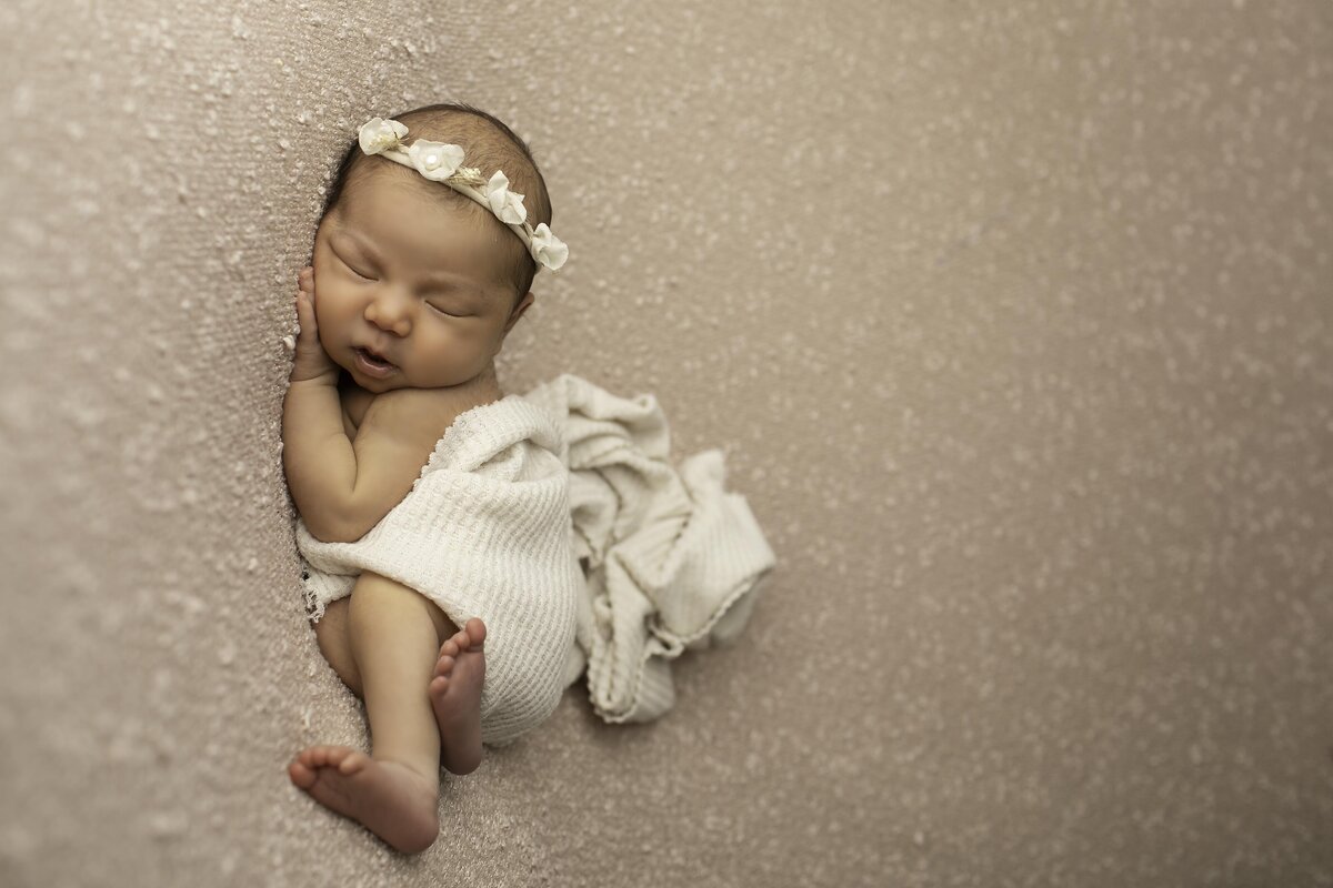 Newborn baby girl peacefully sleeping on a soft mauve backdrop, wrapped delicately with a serene expression, creating a warm and elegant scene