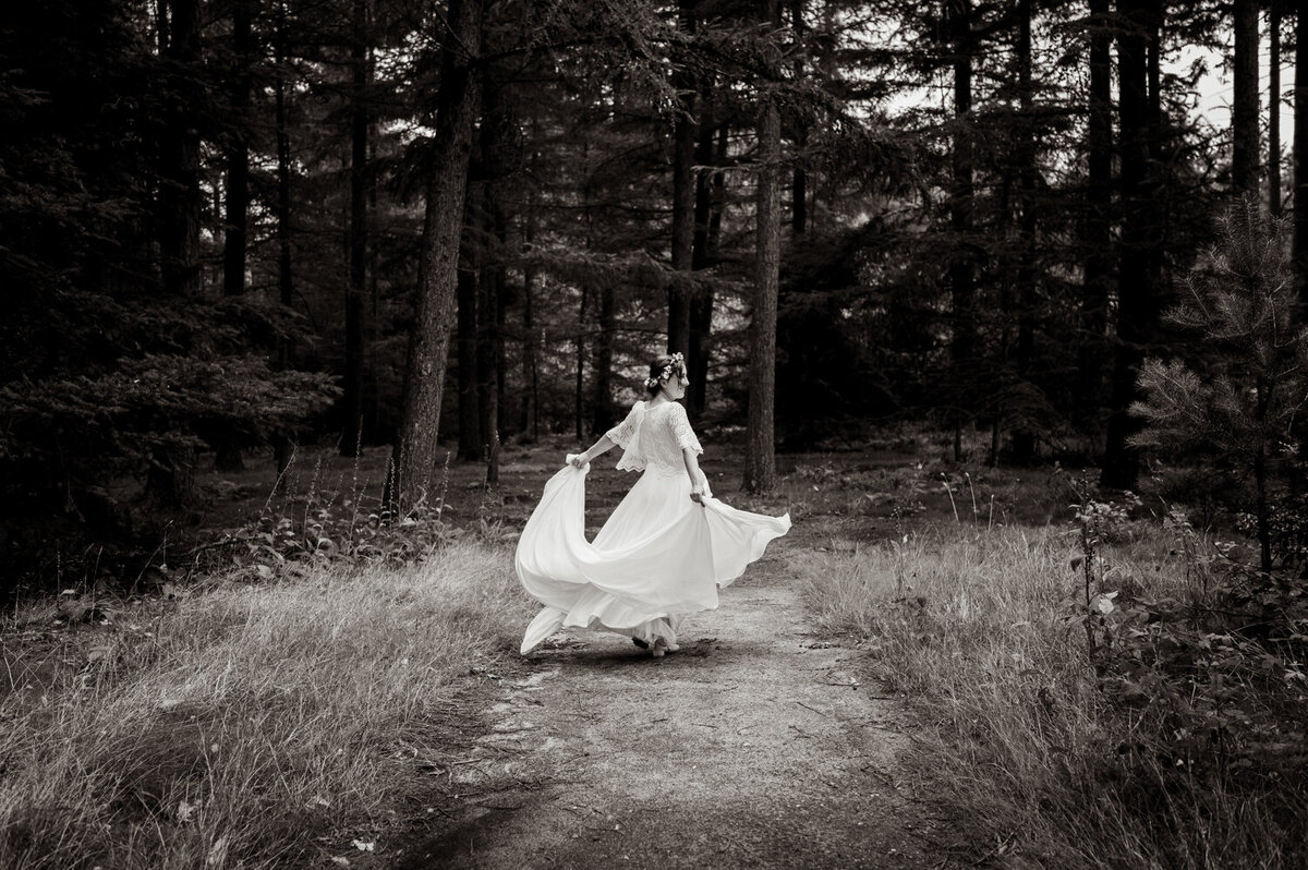 De bruid danst met haar jurk in het bos.