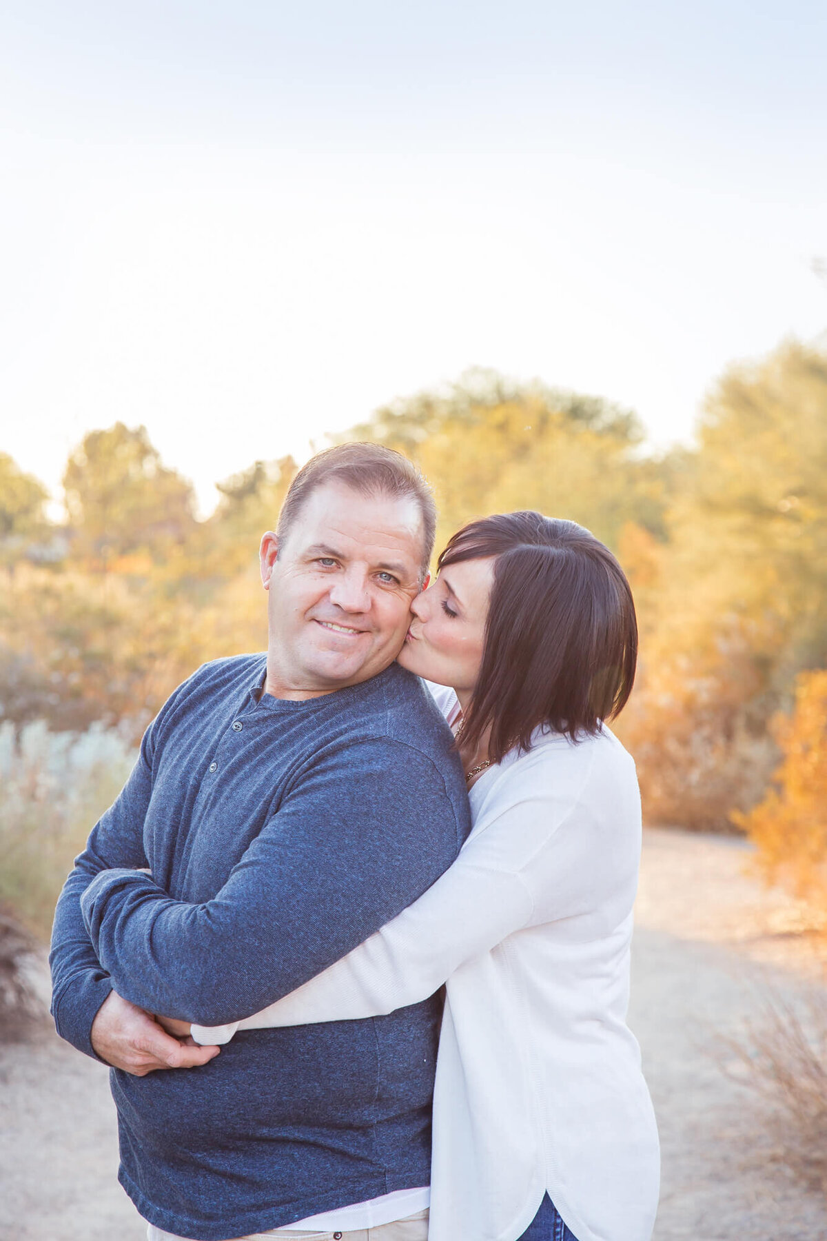 Woman kissing husband on cheek while hugging from behind