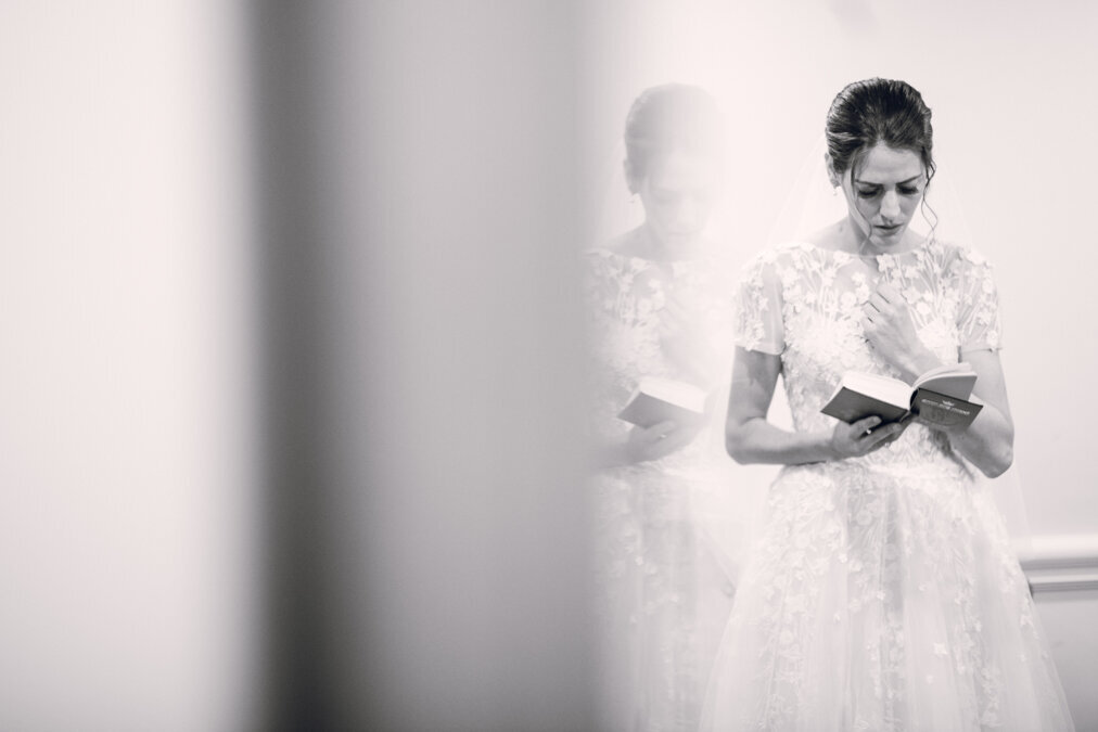 A bride is reading a book in front of a mirror.