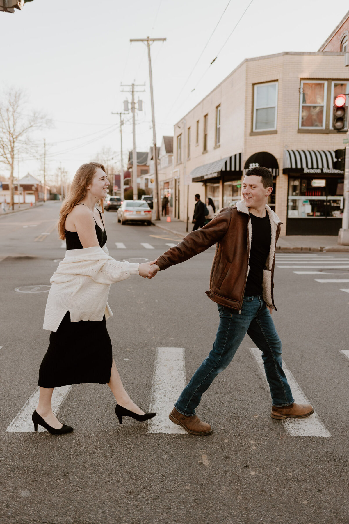 Engaged couple holding hands and crossing the street in Beacon, NY, sharing a playful moment during their engagement photo session.