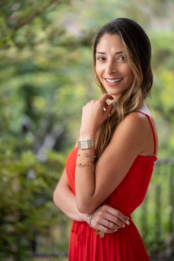 Woman-in-a-red-dress-smiling-outdoors-with-green-foliage-blurred-in-the-background