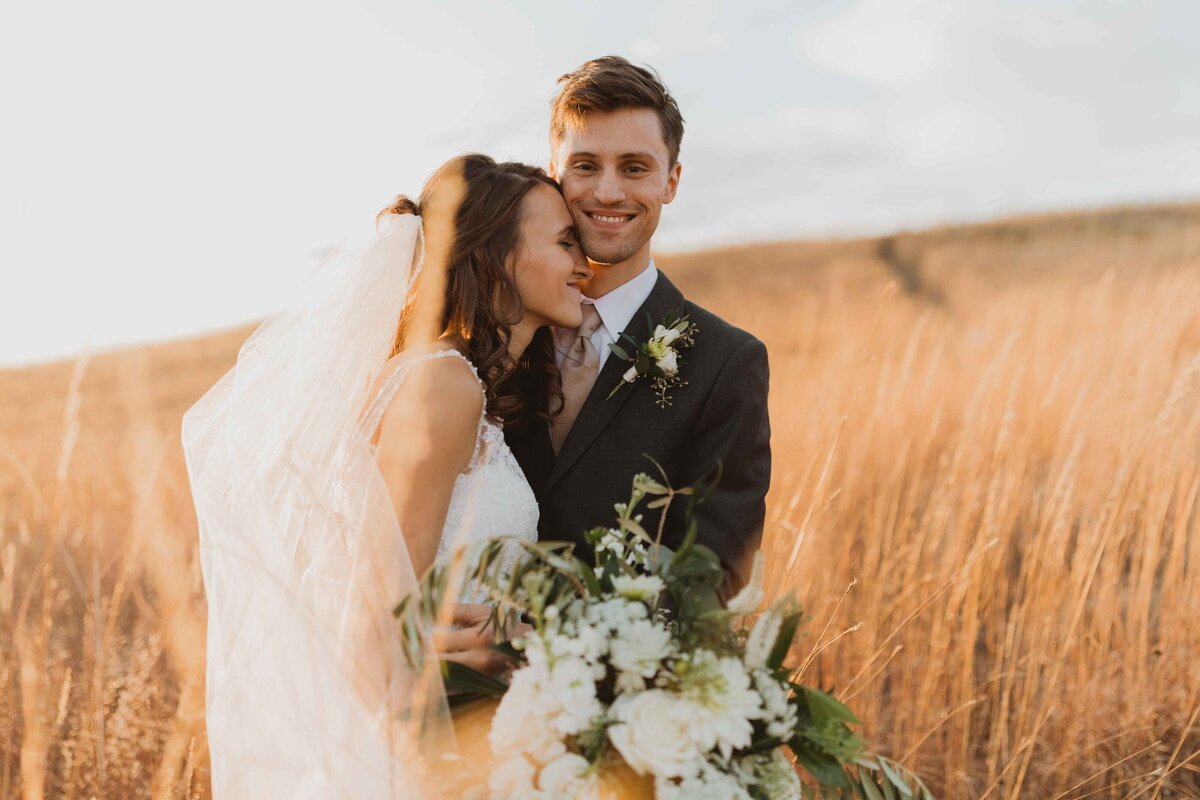 Groom hugging bride outside in Kansas field at sunset in the fall