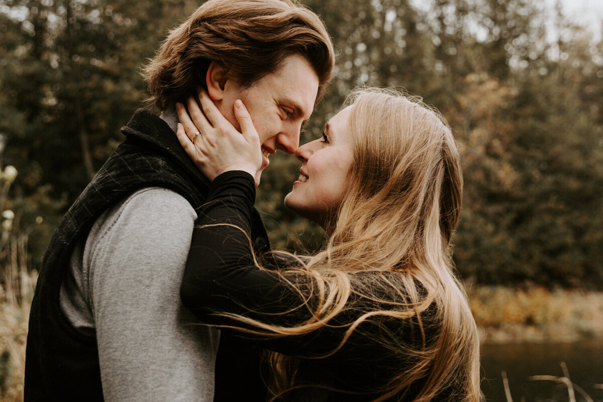 Close up image of man and woman at their engagement photo session. They are facing each other with their noses touching. The woman's hands are on both sides of his face.