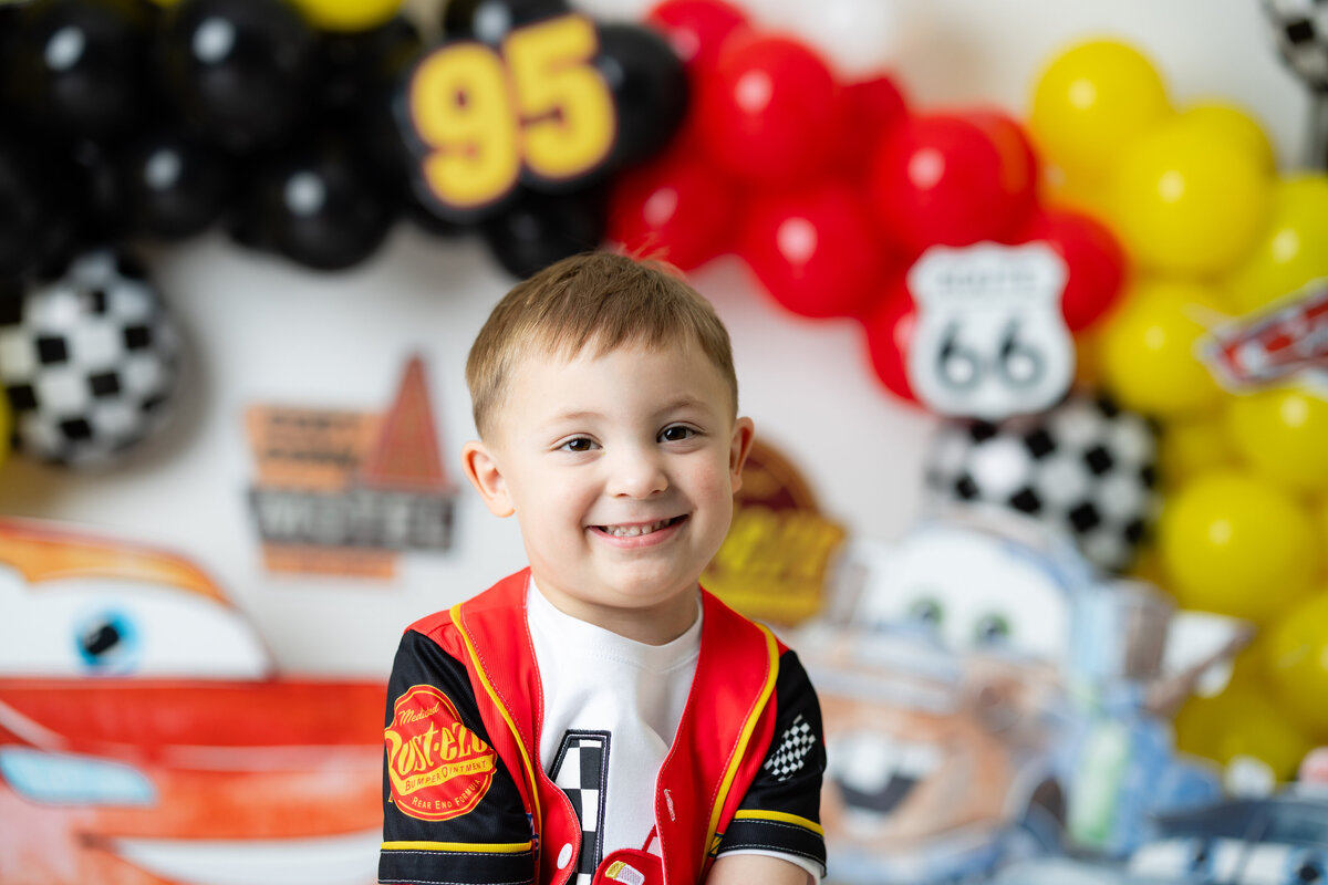 Boy having a high-energy Lightning McQueen-themed birthday session, playing with Cars toys and decorations, captured by Victoria Lee Photography.