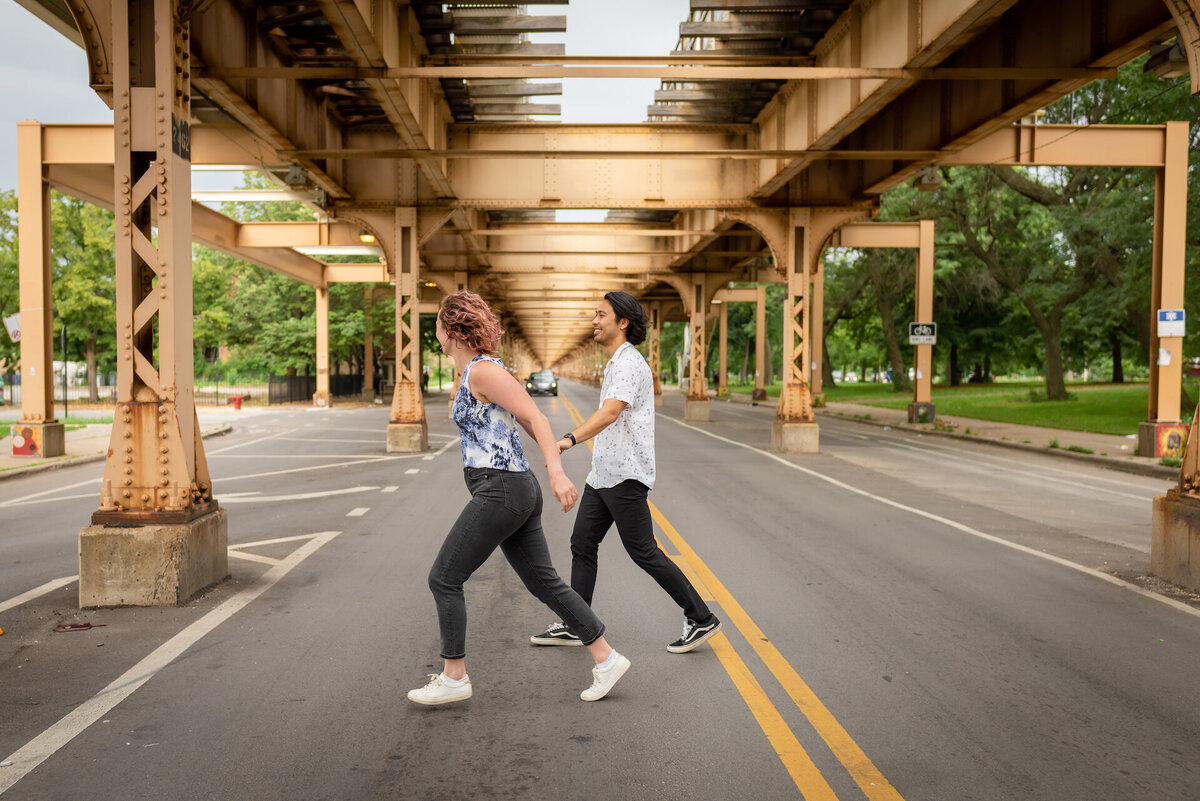 A coouple hold hands while running underneath train tracks in Chicago
